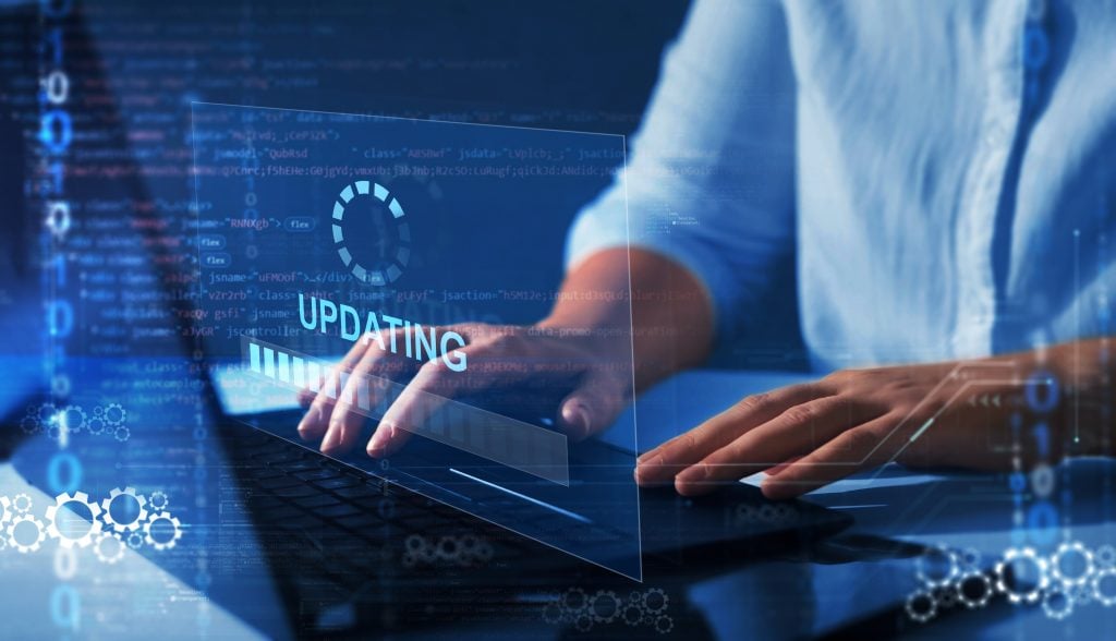 Professional working on a laptop with a futuristic, transparent update interface overlaid on the screen, displaying code and gear icons, emphasizing software or system updating in a high-tech environment.